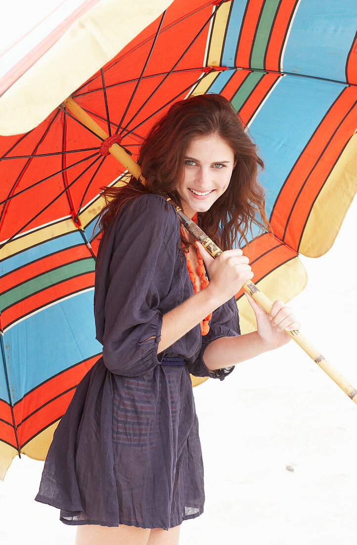 A brunette woman wearing a purple bath robe with a colourful parasol