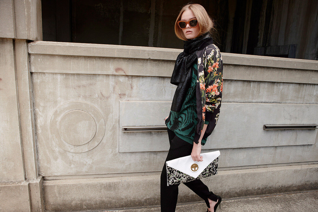 A young blonde woman wearing a jacket with a handbag and sunglasses