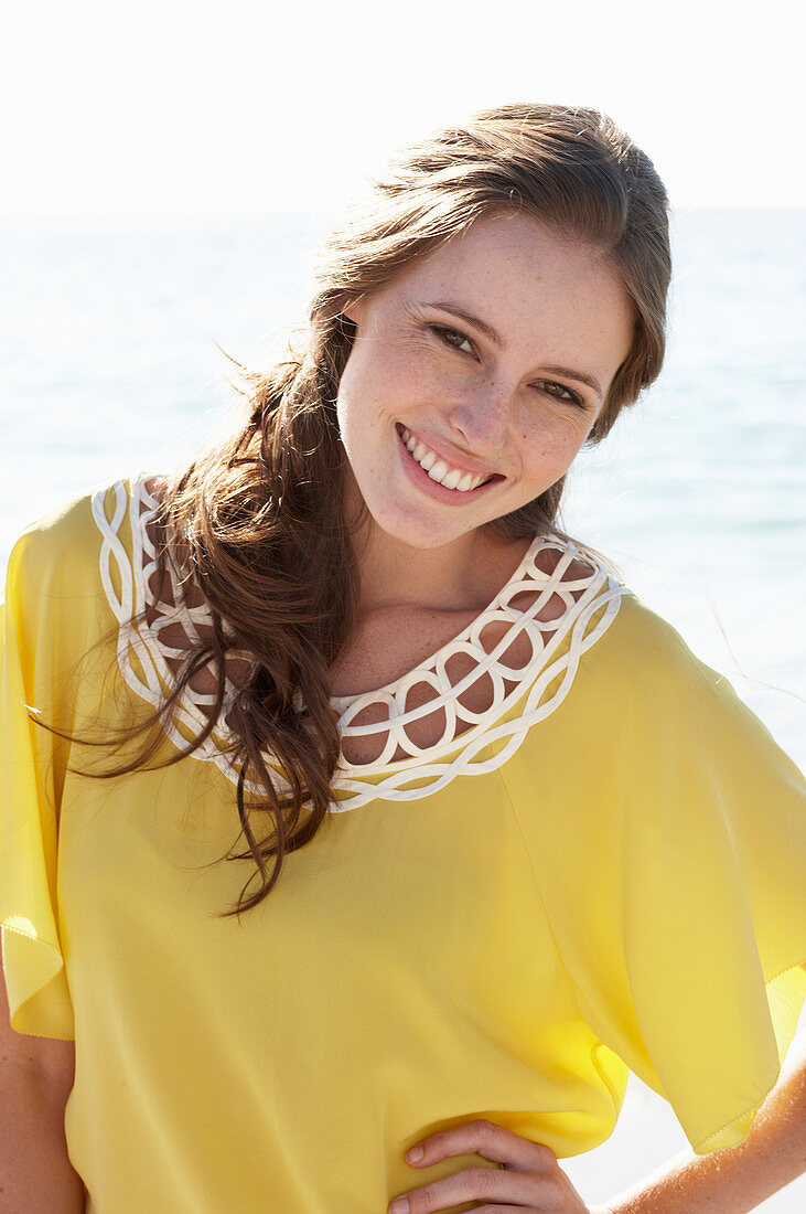 A young brunette woman on a beach wearing a yellow summer dress