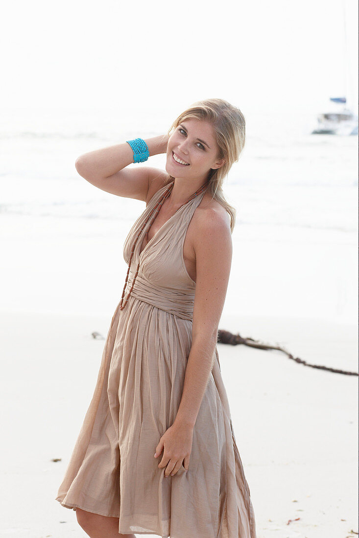 A blonde woman on a beach wearing a beige summer dress