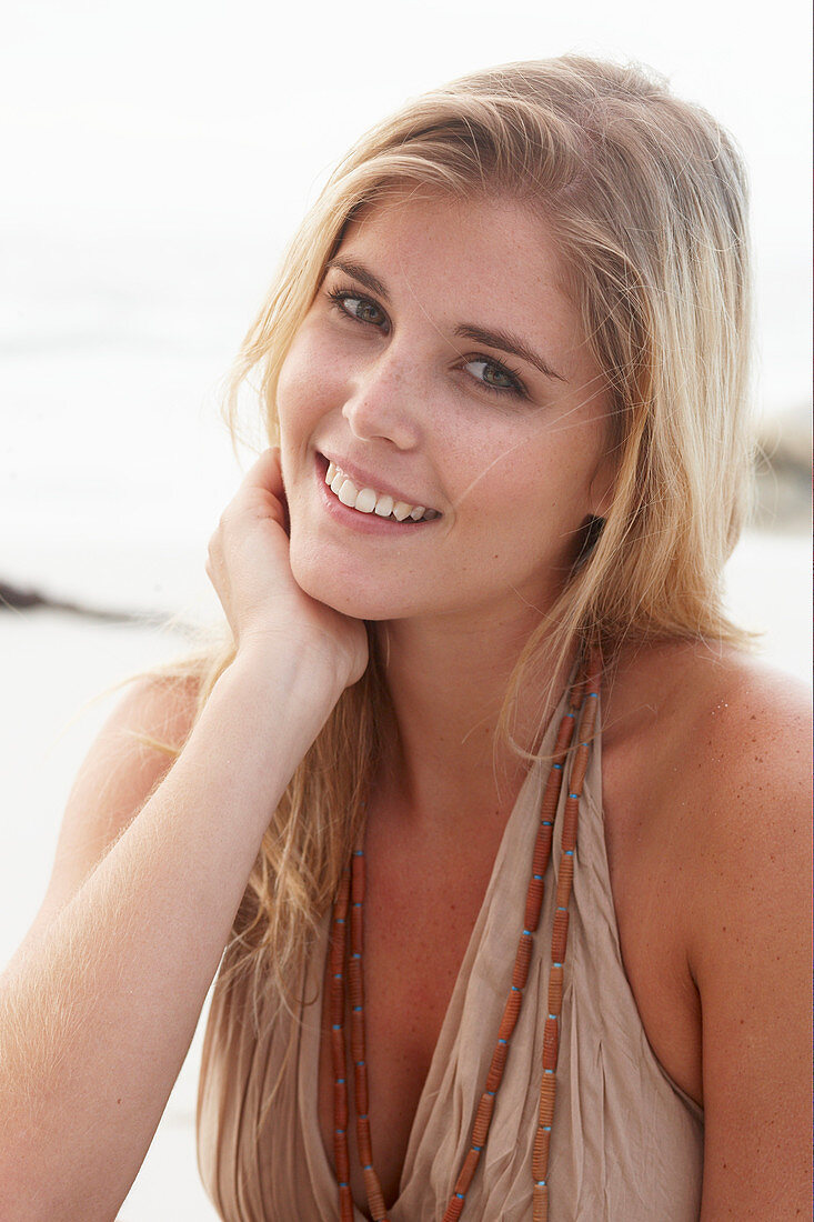 A blonde woman on a beach wearing a beige summer dress