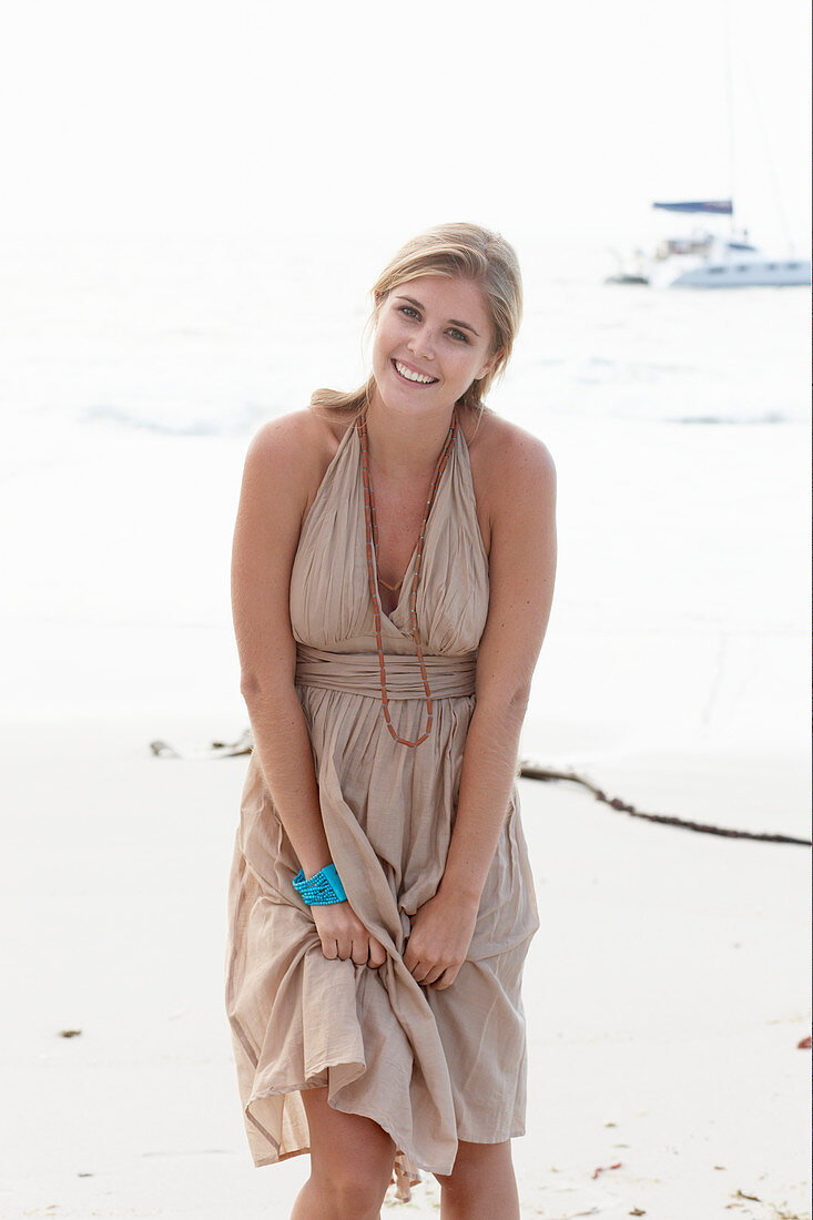 Blonde Frau in beigem Sommerkleid am Strand