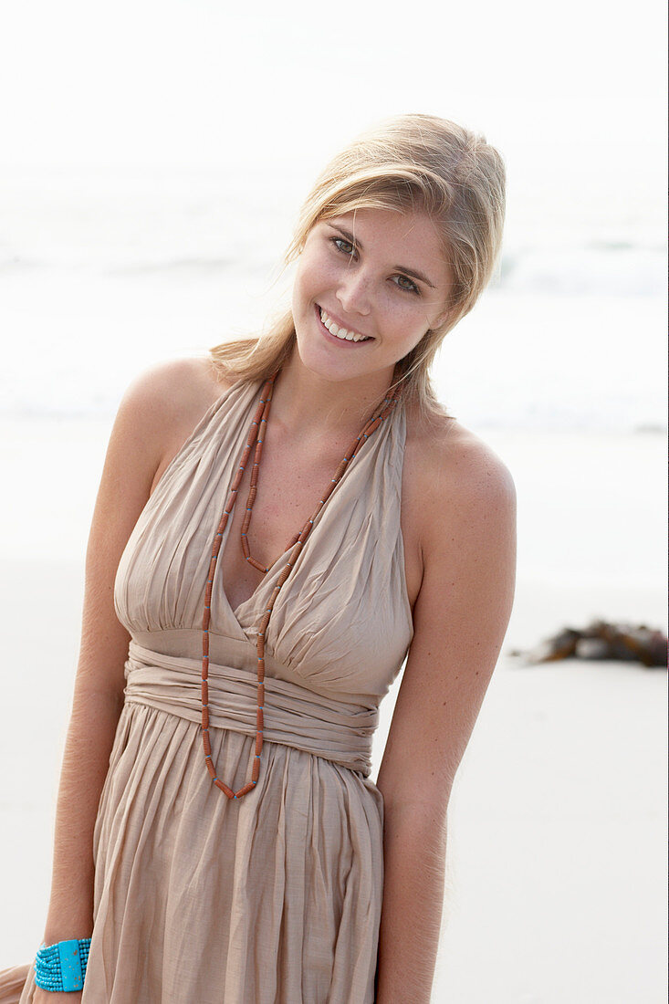 Blonde Frau in beigem Sommerkleid am Strand