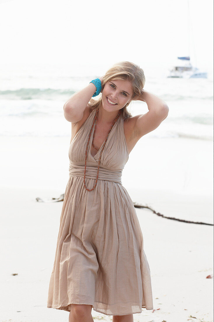 A blonde woman on a beach wearing a beige summer dress