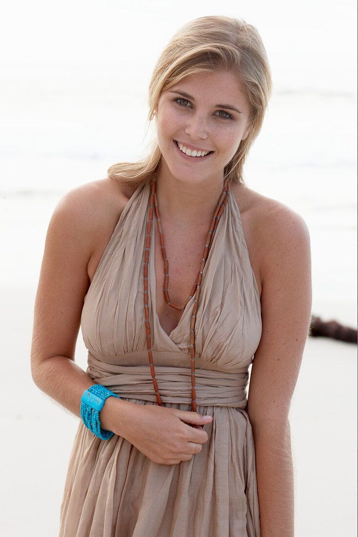 A blonde woman on a beach wearing a beige summer dress