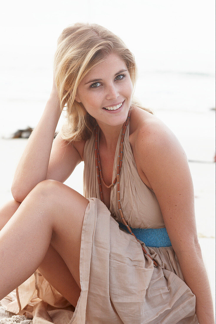 A blonde woman on a beach wearing a beige summer dress