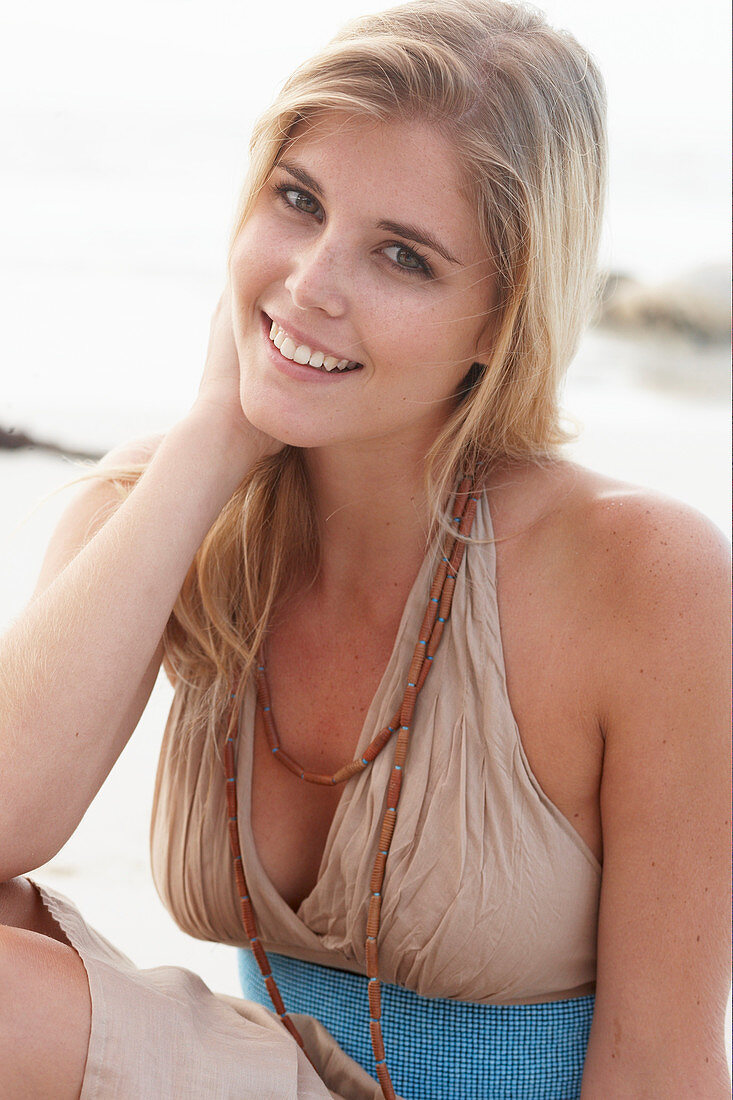 A blonde woman on a beach wearing a beige summer dress