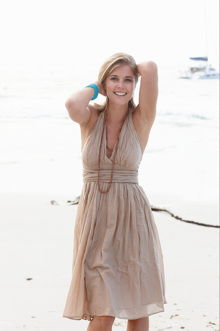 A blonde woman on a beach wearing a beige summer dress