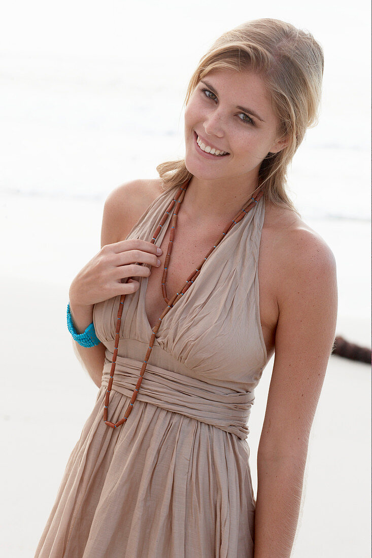 A blonde woman on a beach wearing a beige summer dress