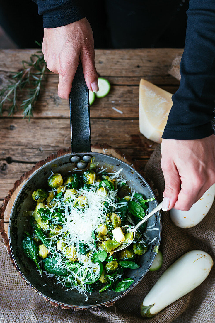 Person holding a spoon inside of the baking pan filled with sprout, baby spinach and parmesan