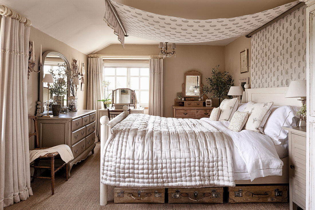 Old suitcases under double bed with canopy and silk bedspread