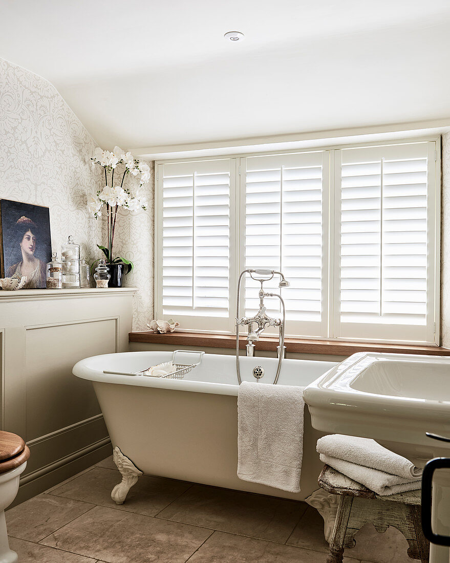 Free-standing bathtub below window with closed shutters and oil painting on ledge