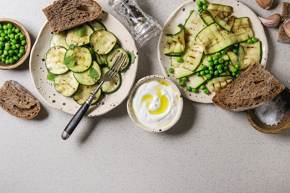 Variety of grilled zucchini salad with green pea, yogurt dip, garlic and rye sliced bread in spotted ceramic plates