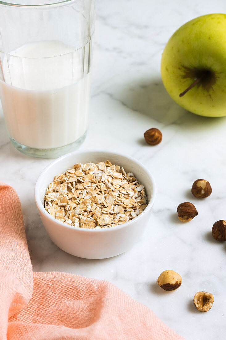 Oat bowl with hazelnuts, an apple and a glass of milk