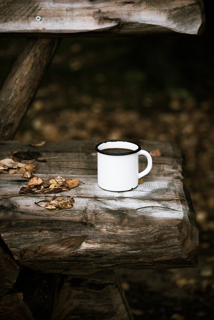 An enamel mug of coffee on a rustic wooden bench