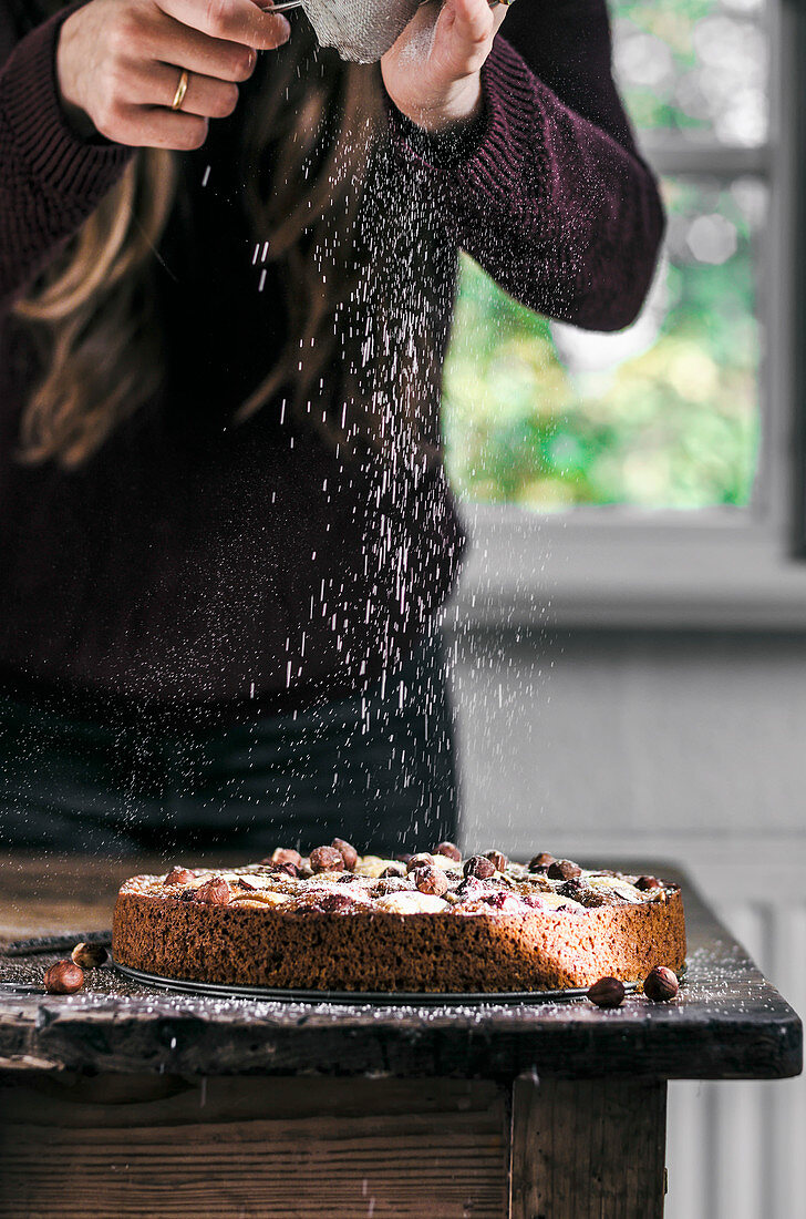 A woman dusting a vegan Apple Hazelnut Cake with sugar