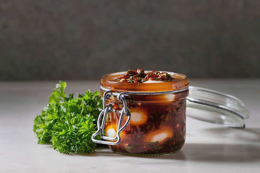 Opened Jar with homemade pickled marinated quail eggs in tomato and olive oil sauce with anchovies and fresh parsley