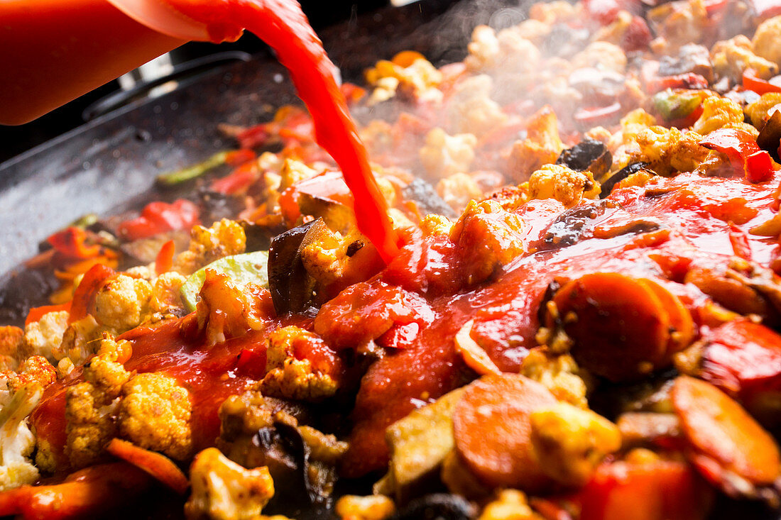 Preparing vegan paella: add the tomato sauce