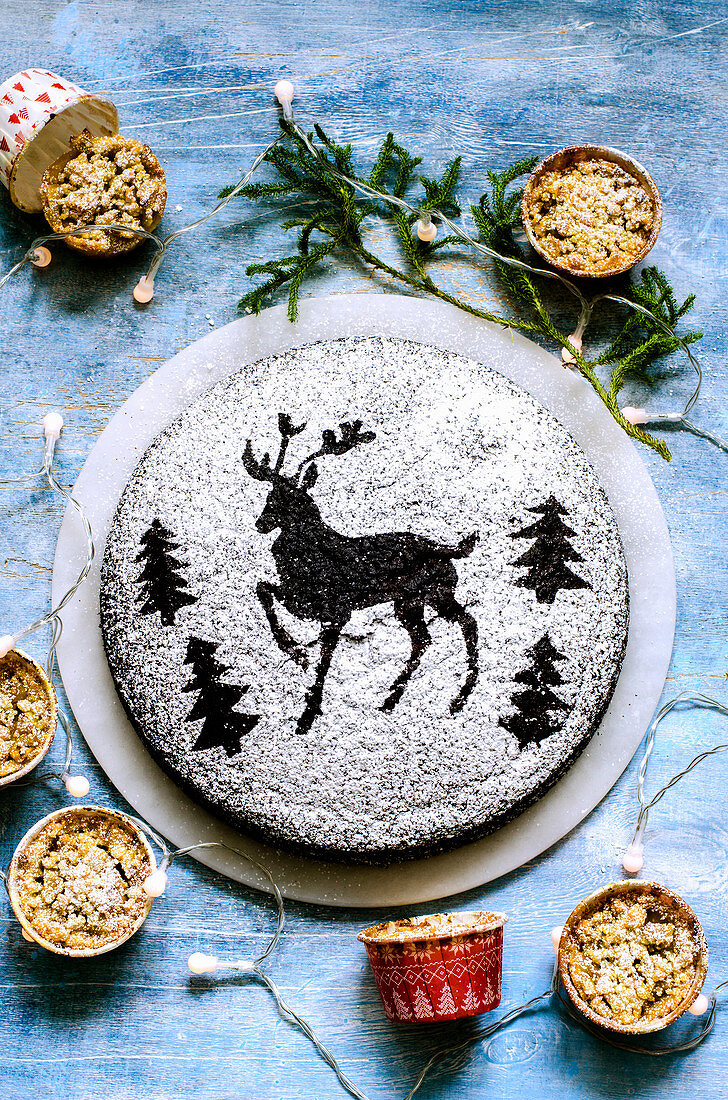 Chocolate cake dusted with icing sugar through a stencil of deer and Christmas trees