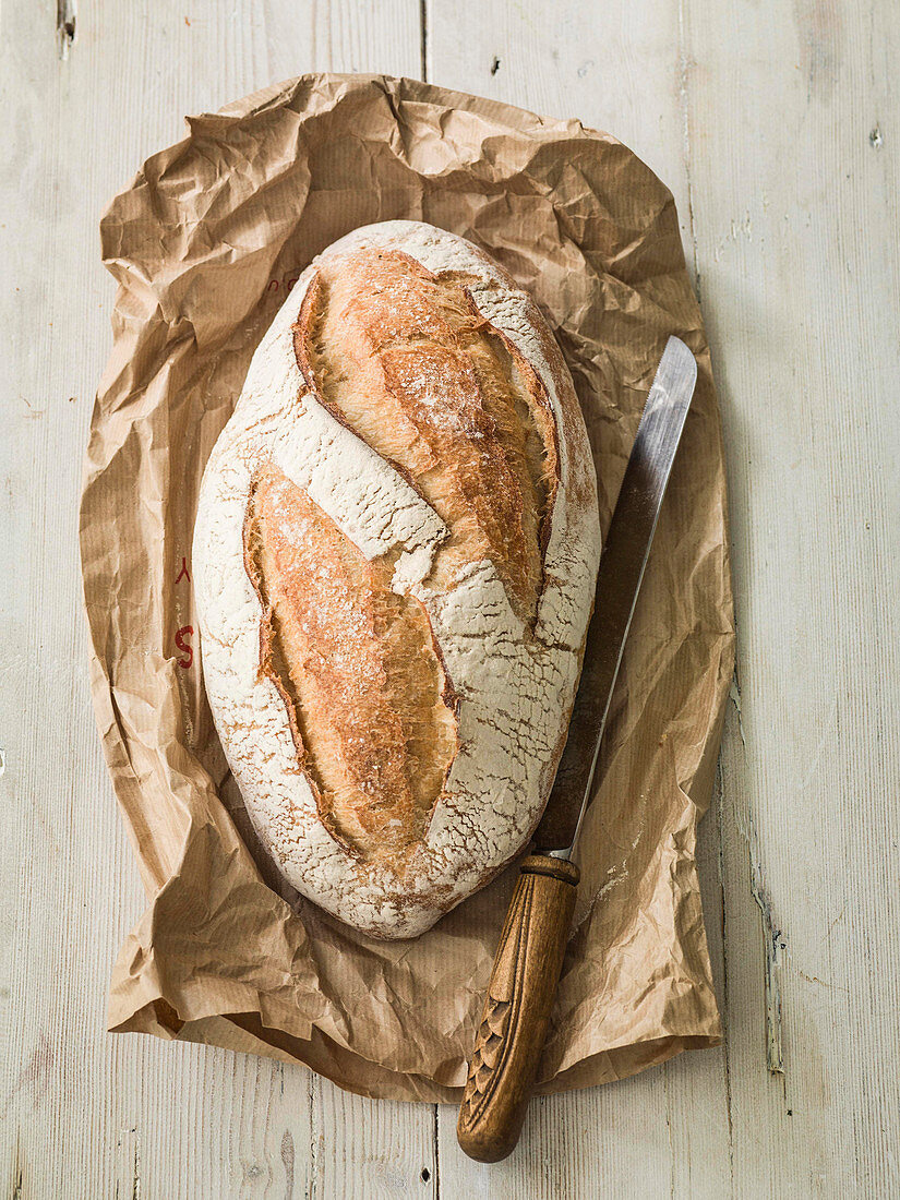 French Sourdough bread loaf with bread knife on paper wrapper