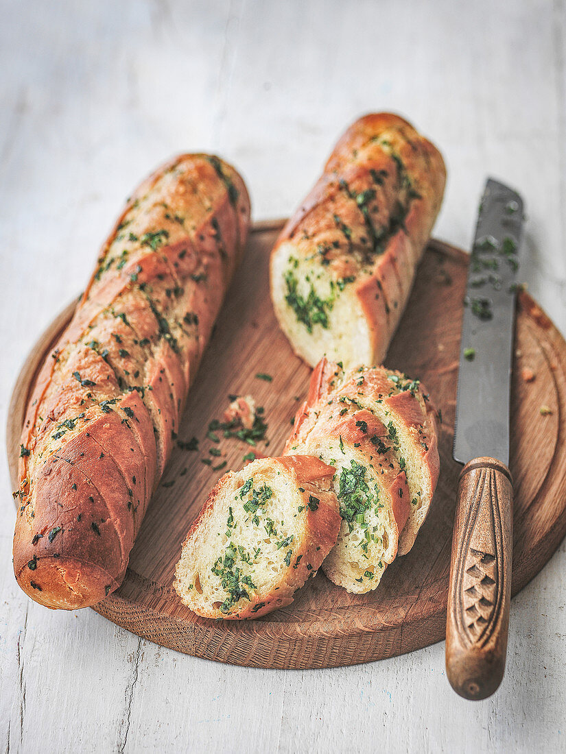 Garlic and herb bread cut on board with knife