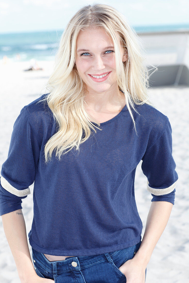 A young blonde woman on a beach wearing a long-sleeved blue shirt