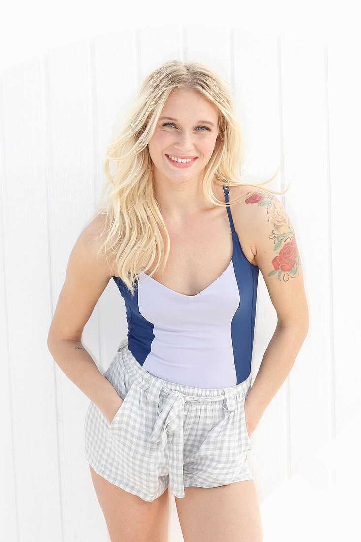 A young blonde woman with a tattoo wearing a bathing suit and shorts