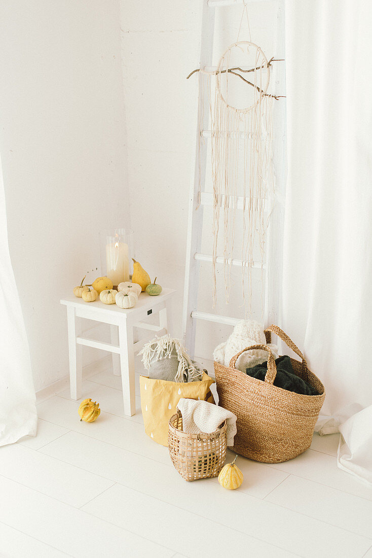 Pale, modern, autumn arrangement of pumpkins, ladder on wall, dreamcatcher and baskets