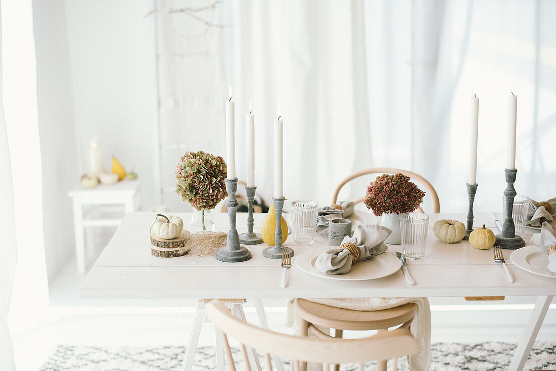 Autumnal arrangement of hydrangeas, pumpkins and candlesticks on table