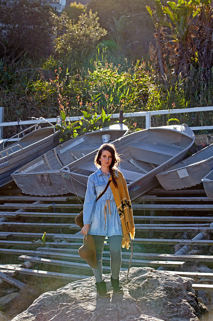 A young woman wearing a Western-style outfit consisting of a long, denim shirt and a poncho with a bag and a hat