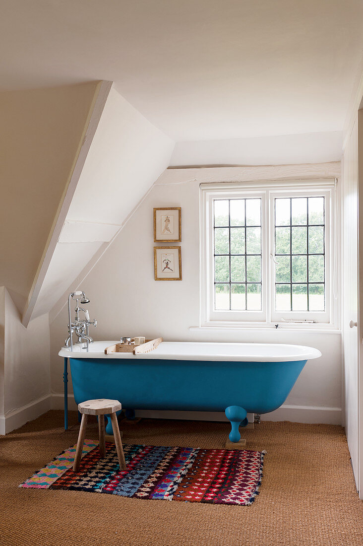 Free-standing bathtub, Moroccan rug and wooden stool in rustic bathroom