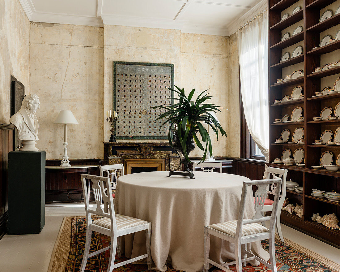 English china on ceiling height shelves in dining room with white american 19c chairs, artwork and rug