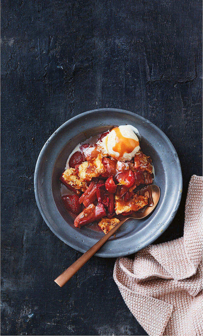 Kuchenauflauf mit Rhabarber, Erdbeeren, Eiscreme und Karamellsauce auf Teller