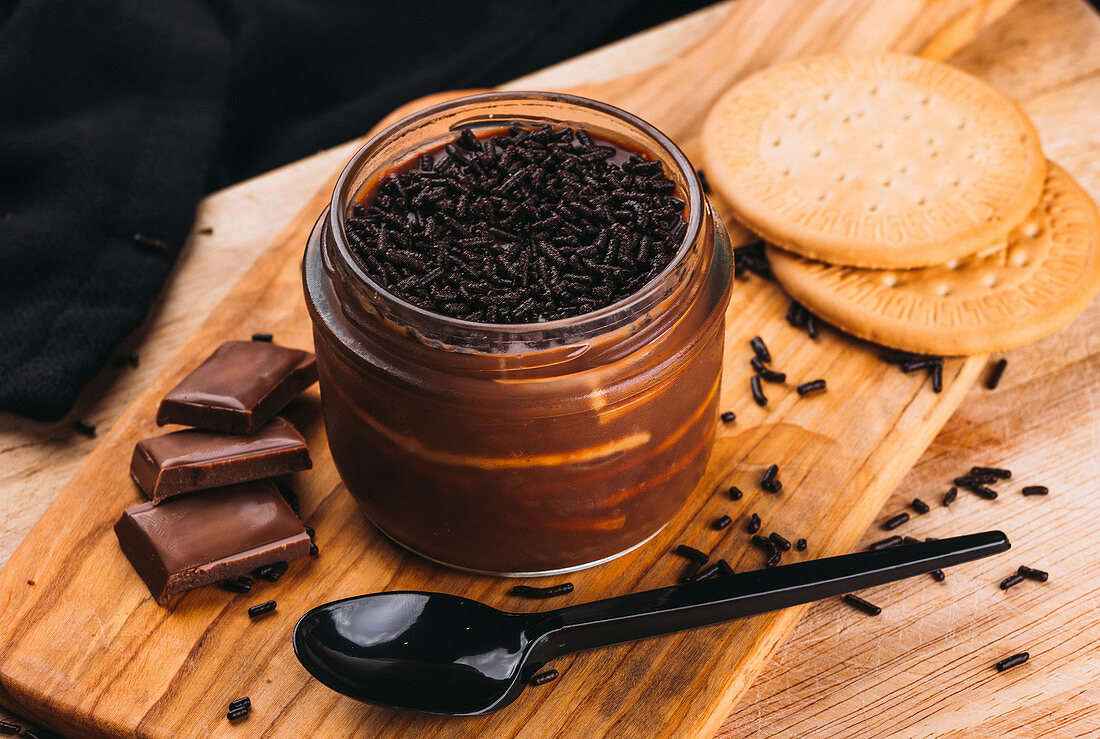 Close-up shot of board with served cookies and jar of sweet mousse dessert with chocolate topping