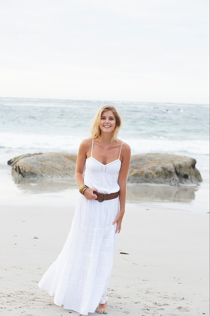 A blonde woman by the sea wearing a white summer dress