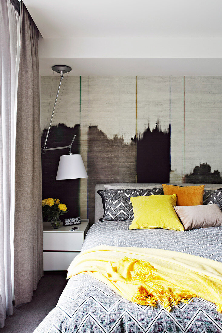 Double bed, bedside table and lamp in the bedroom with textile wallpaper on the wall