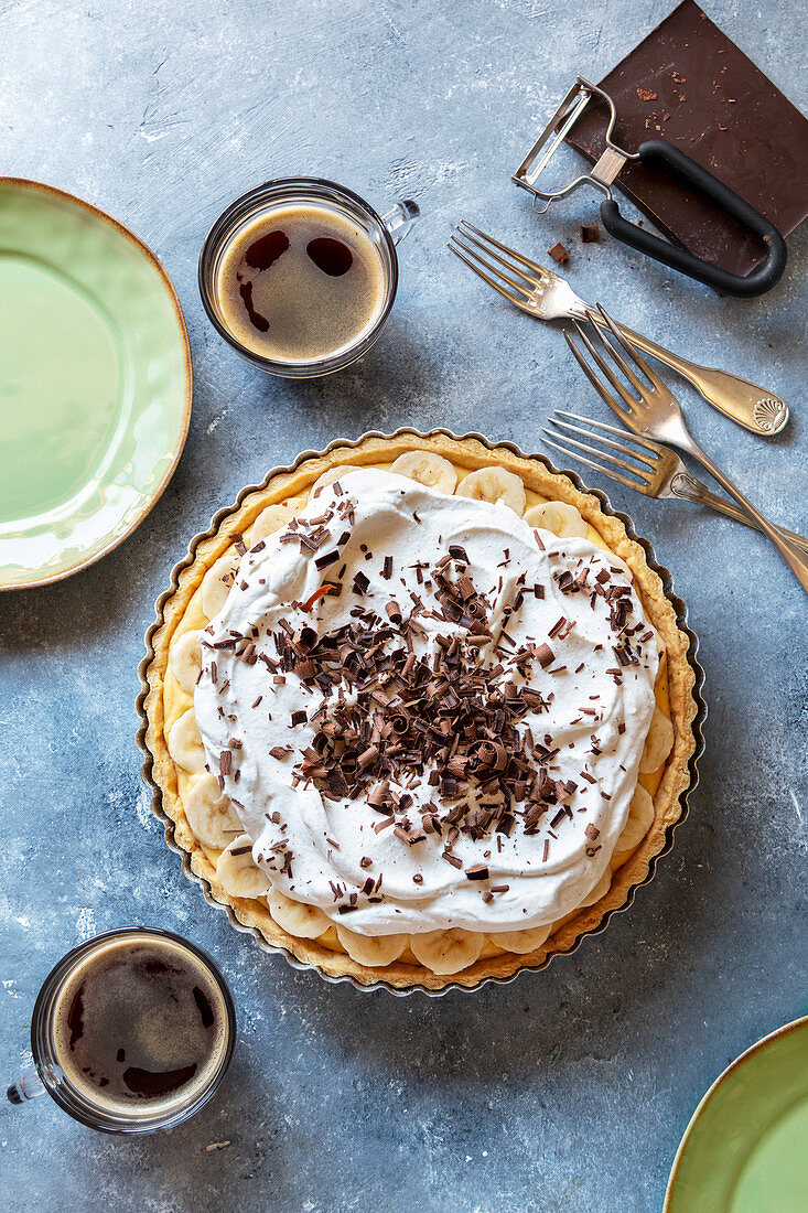 Banana cream pie decorated with chocolate curls and 2 cups of coffee on the table