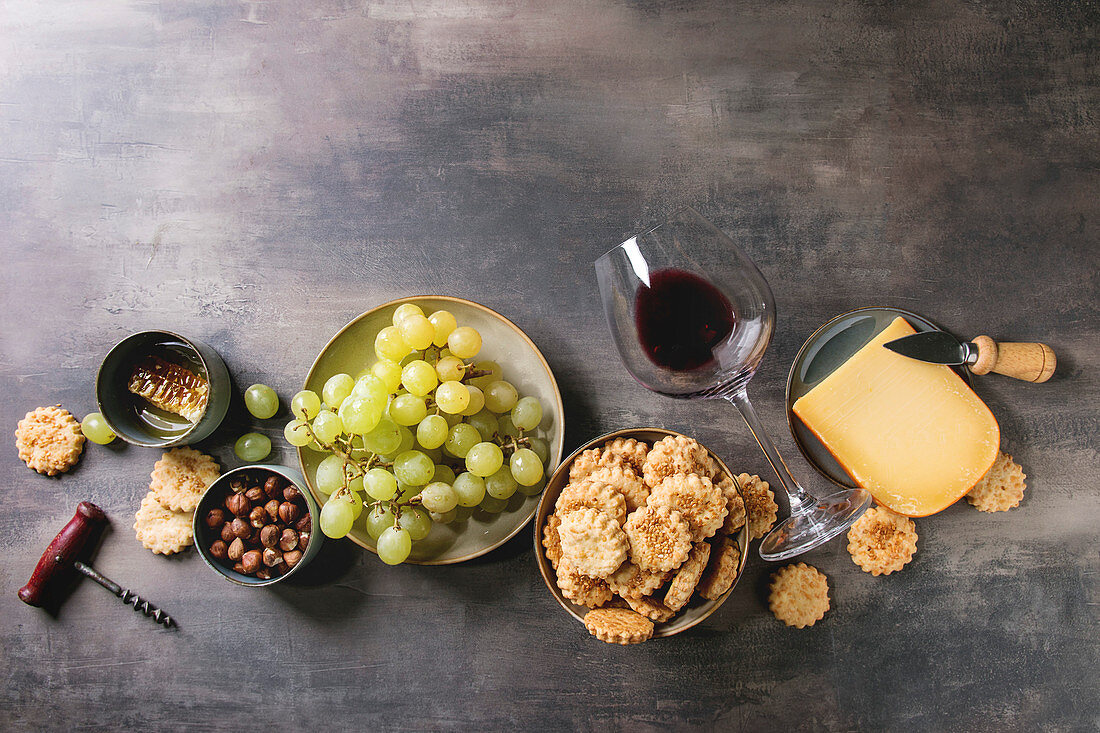 Cheese, grapes, nuts, cheese crackers cookies, honeycombs with laying glass of red wine and knife over dark background