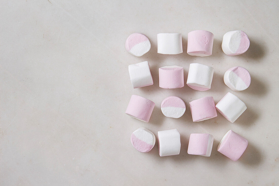 Weiß-rosa Marshmallows in Viererreihen auf weißem Untergrund