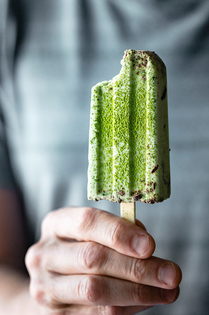 Person hält ein Matcha-Stieleis mit Minzschokolade in der Hand