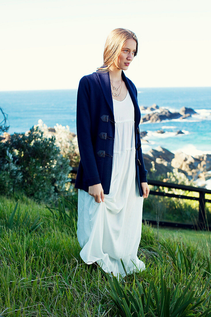 A young brunette woman wearing a jacket and a summer dress standing in the grass