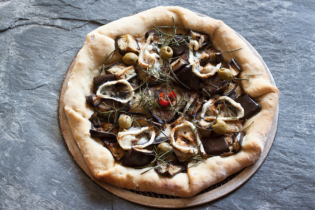 Pizza topped with eggplant, goat's cheese, rosemary, red pepper and green olives