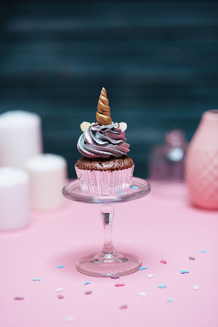 A muffins with pastel coloured frosting decorated with a unicorn horn