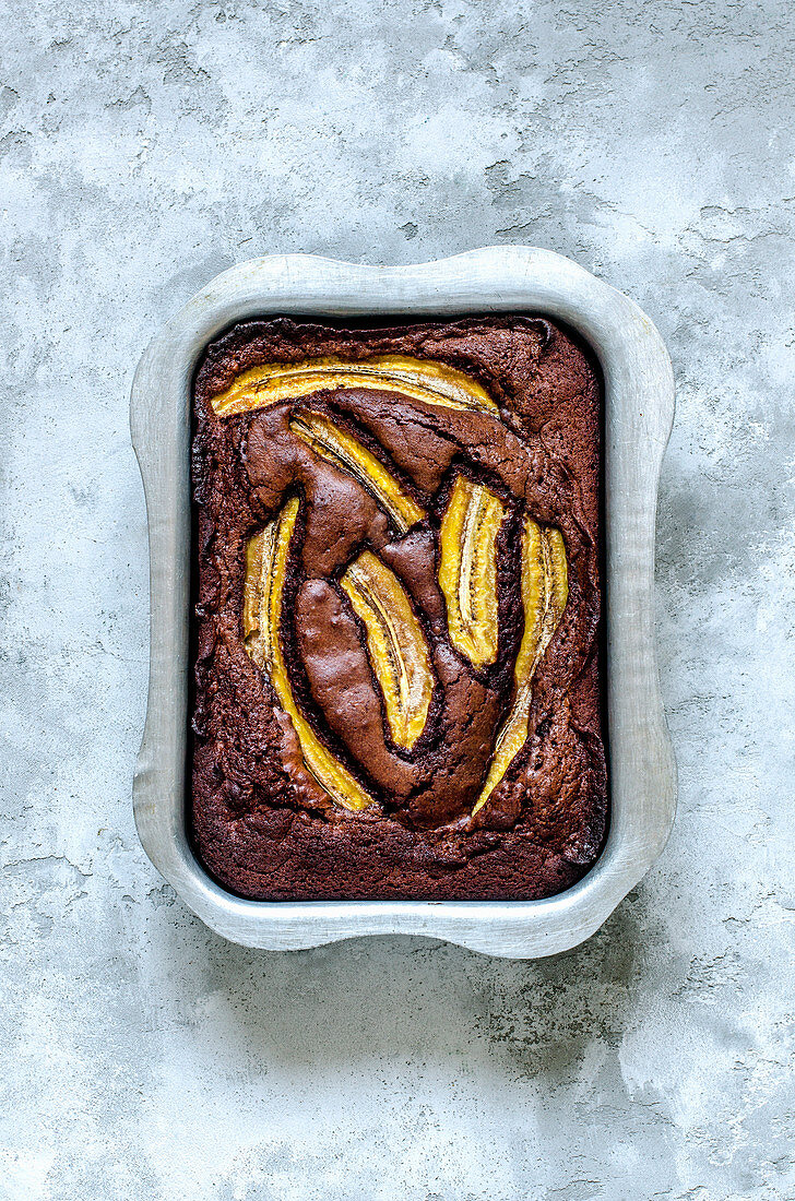 Brownie with milk chocolate, bananas and sea salt in aluminum form on a concrete surface