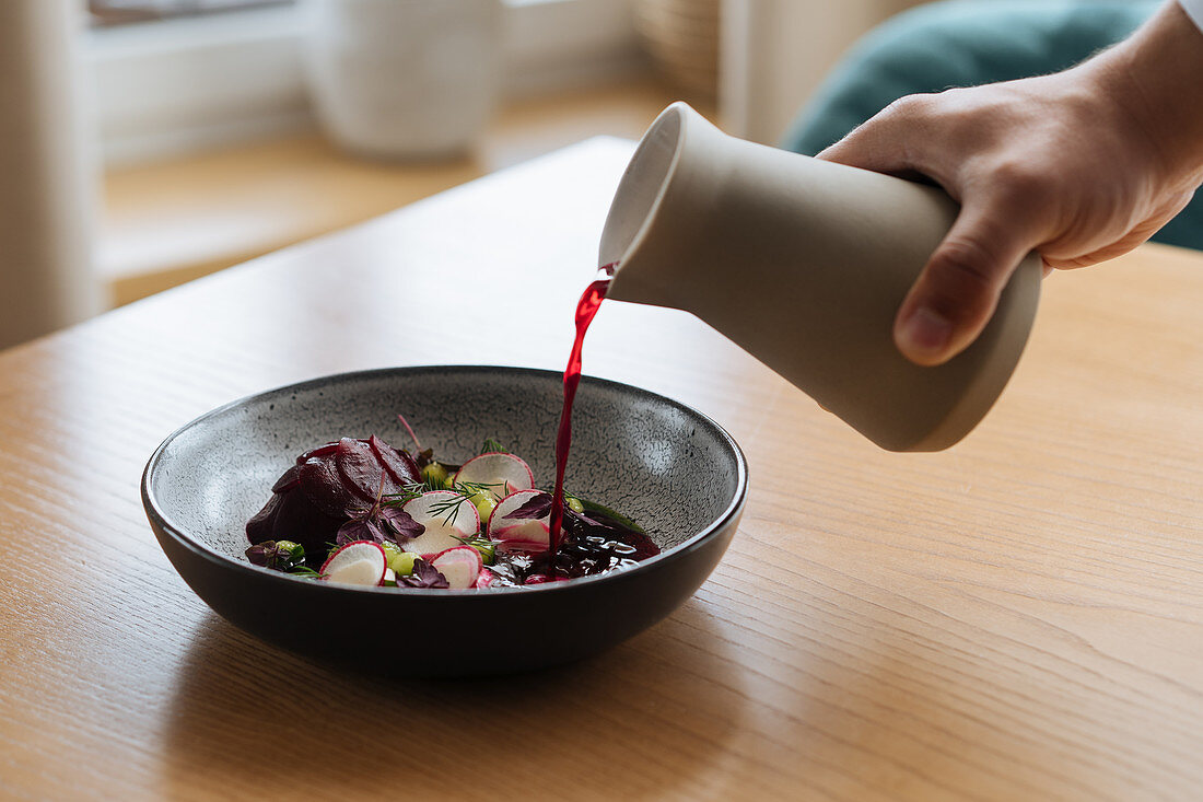 Warm beetroot juice being poured over sliced vegetables