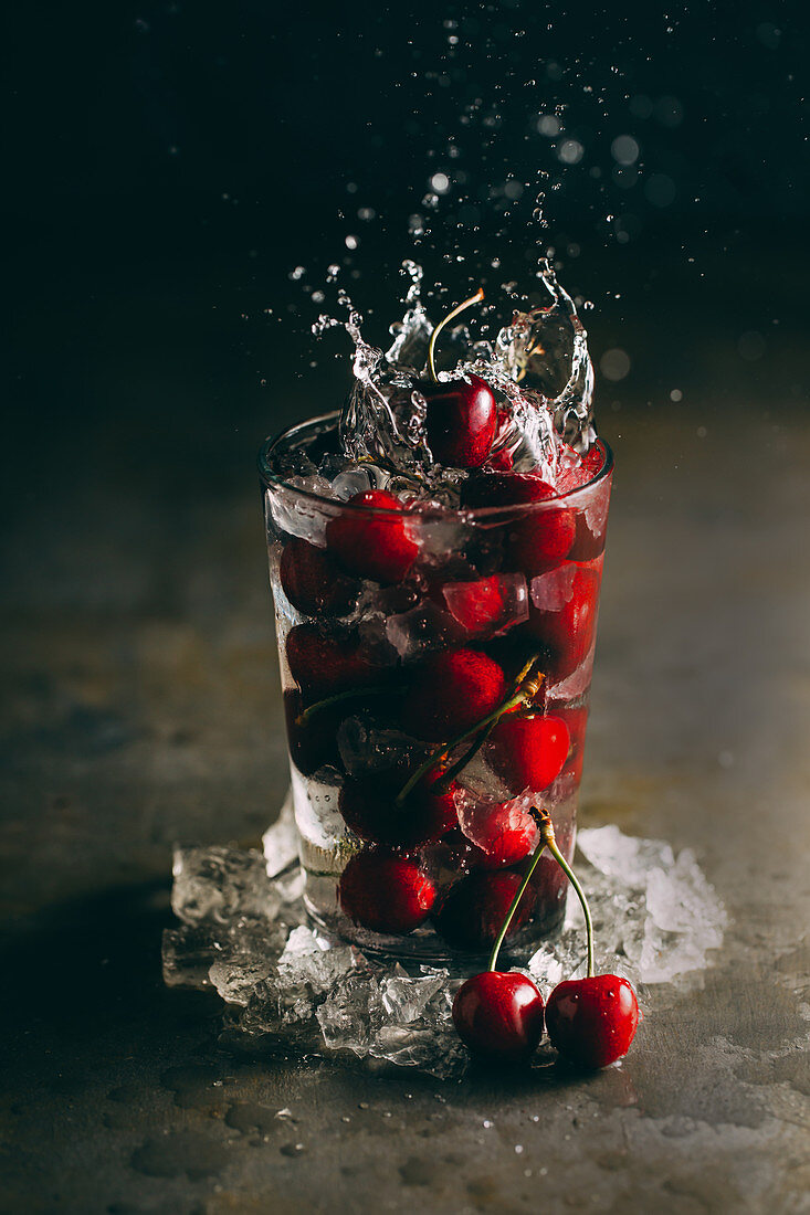 Cherries falling into a glass of iced water