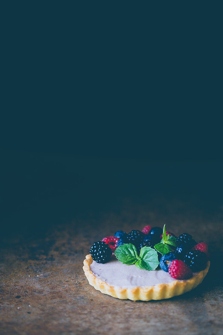 A berry cake with mint against a dark surface