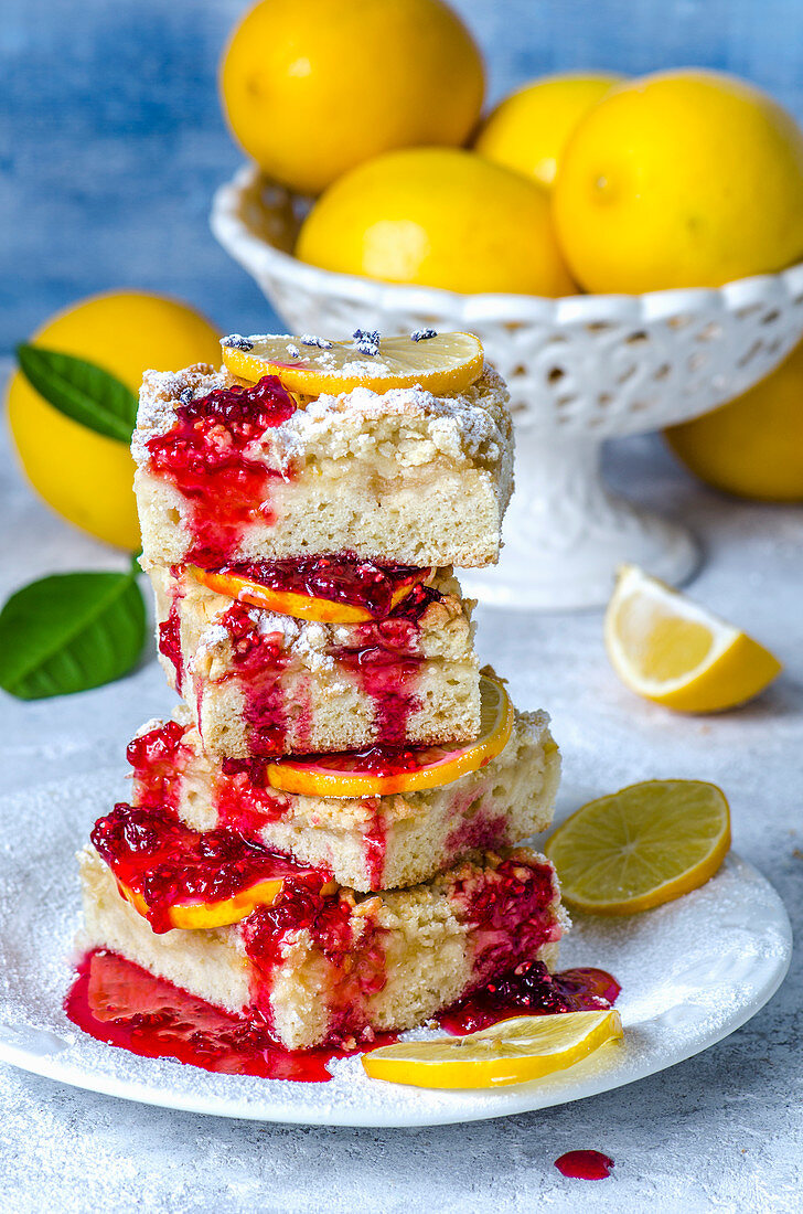 Lemon pie cut by squares, poured with raspberry sauce, decorated with lemon slices and fresh lemons