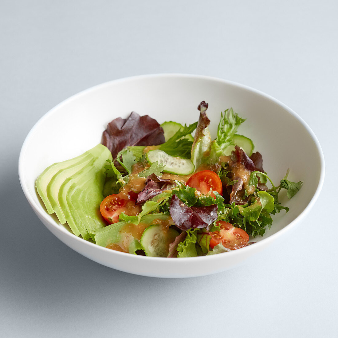 A mixed salad with cucumber and tomatoes in a bowl against a white surface