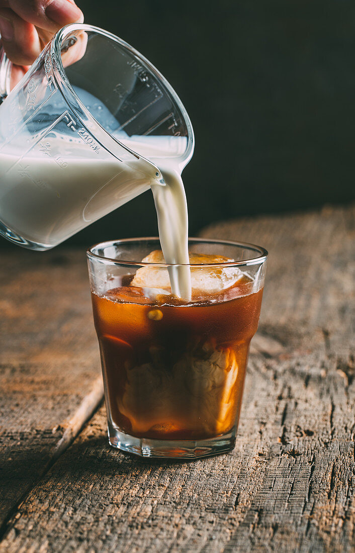 Milk being poured into a glass of ice cold coffee